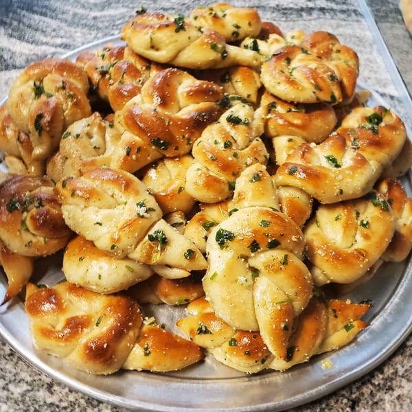 A silver platter piled high with golden-brown La Bella Italia garlic knots, sprinkled with herbs and salt.