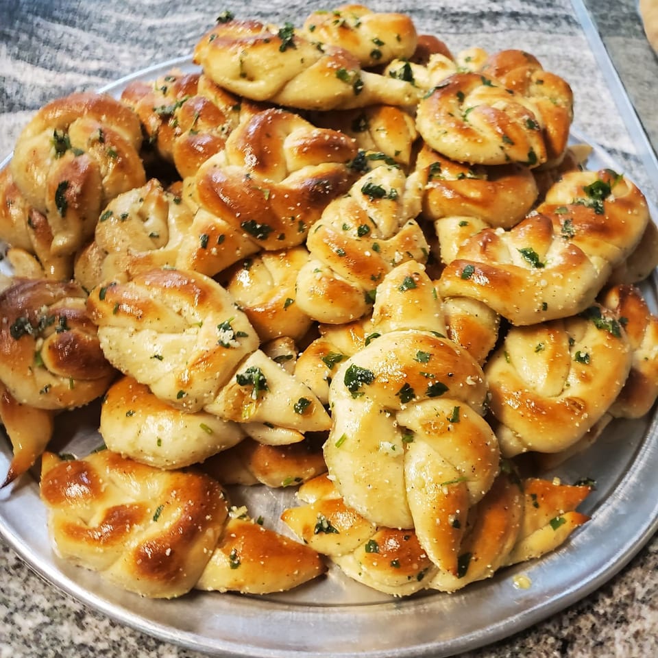 A silver platter piled high with golden-brown La Bella Italia garlic knots, sprinkled with herbs and salt.