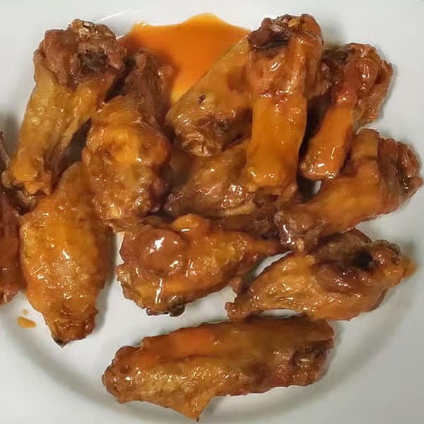 A white plate filled with golden-brown chicken wings, generously coated in a glossy orange sauce.